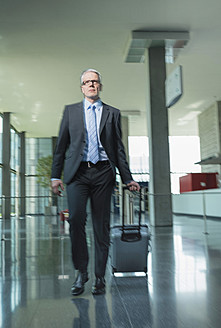 Germany, Stuttgart, Businessman pulling luggage in office building - MFPF000207