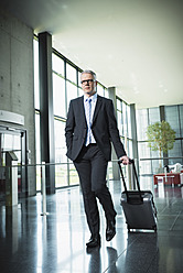 Deutschland, Stuttgart, Geschäftsmann beim Kofferziehen im Bürogebäude - MFPF000208