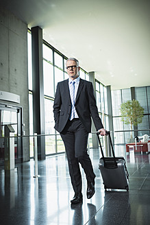 Germany, Stuttgart, Businessman pulling luggage in office building - MFPF000208