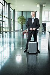 Deutschland, Stuttgart, Geschäftsmann stehend mit Gepäck in Bürogebäude - MFPF000210