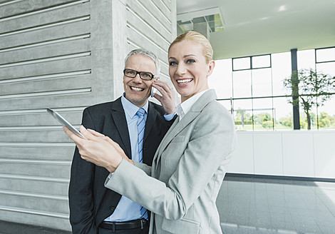 Germany, Stuttgart, Businesswoman with digital tablet while man talking on phone - MFPF000234