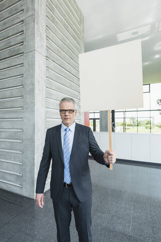 Deutschland, Stuttgart, Geschäftsmann hält Plakat in Bürohalle, lizenzfreies Stockfoto