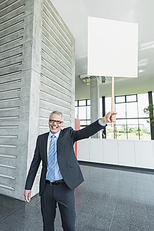 Germany, Stuttgart, Businessman holding placard in office lobby - MFPF000240