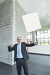 Deutschland, Stuttgart, Geschäftsmann hält Plakat in Bürohalle - MFPF000241