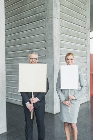Deutschland, Stuttgart, Geschäftsleute halten leere Schilder in einer Bürohalle, lächelnd, Porträt, lizenzfreies Stockfoto