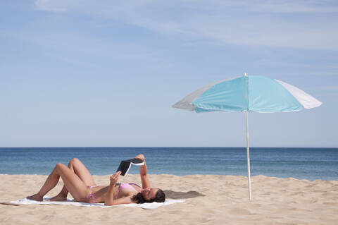 Portugal, Lagos, Mittlere erwachsene Frau liest Buch am Strand, lizenzfreies Stockfoto