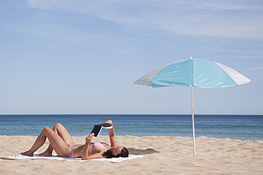 Portugal, Lagos, Mittlere erwachsene Frau liest Buch am Strand - UMF000355