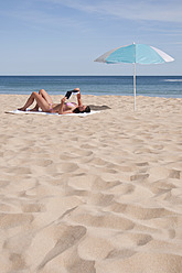 Portugal, Lagos, Mittlere erwachsene Frau liest Buch am Strand - UMF000356