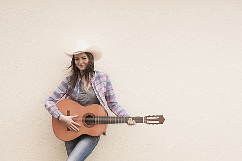 Deutschland, Nordrhein-Westfalen, Junge Frau mit Cowboyhut spielt akustische Gitarre, lächelnd - KJF000163