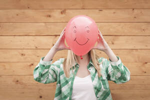 Deutschland, Nordrhein-Westfalen, Jugendliches Mädchen bedeckt Gesicht mit Smiley-Ballon - KJF000165