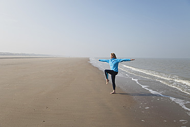 Belgien, Reife Frau in Baum-Pose an der Nordsee stehend - GWF001882