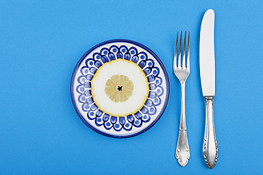 Zitronenscheibe auf Teller mit Gabel und Messer - GWF001888