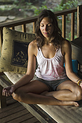 Indonesien, Junge Frau meditiert auf der Veranda - MBEF000439