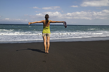 Indonesia. Young woman standing on black sand - MBEF000444