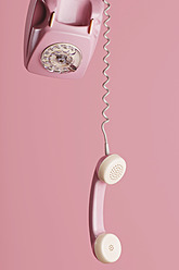 Altmodisches rosa Wählscheibentelefon mit hängendem Hörer vor rosa Hintergrund - LRF000559