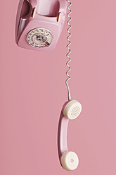 Old fashioned pink dial telephone with hanging receiver against pink background - LRF000559