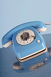 Old fashioned blue telephone reflecting on glass table, close up - LRF000557