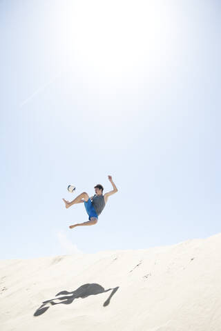 Frankreich, Jugendlicher springt nach Fußball auf Sanddüne, lizenzfreies Stockfoto