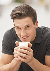 Germany, Young man with coffee cup, smiling, portrait - WBF001463