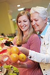 Deutschland, Köln, Frauen mit Smartphone und Orangen im Supermarkt - RKNF000020