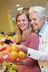 Germany, Cologne, Womens with smart phone and oranges in supermarket - RKNF000020