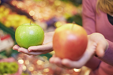 Deutschland, Köln, Junge Frau vergleicht Äpfel im Supermarkt - RKNF000024