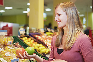 Deutschland, Köln, Junge Frau vergleicht Äpfel im Supermarkt - RKNF000025