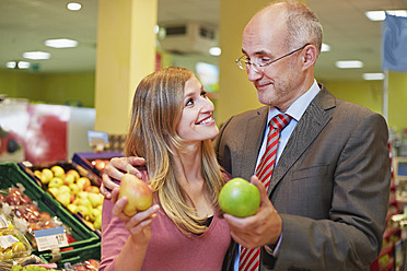 Germany, Cologne, Man and woman with apple and pear in supermarket, smiling - RKNF000028