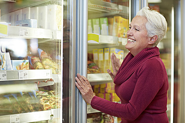 Deutschland, Köln, Reife Frau steht vor Tiefkühltruhe im Supermarkt - RKNF000080
