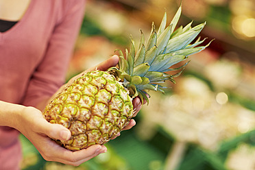 Germany, Cologne, Young woman with pineapple in supermarket - RKNF000101