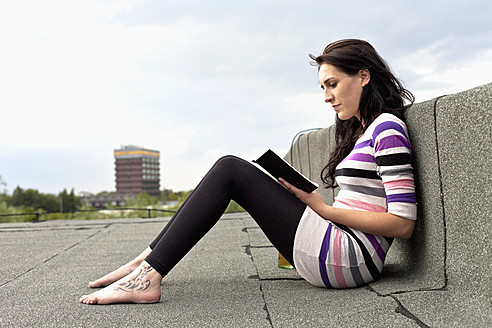 Deutschland, Hamburg, Junge Frau sitzt auf dem Dach und liest ein Buch - DBF000199