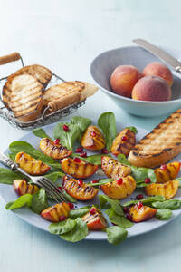 Pfirsichsalat garniert mit Granatapfelkernen und Kräutern auf dem Teller - ECF000065