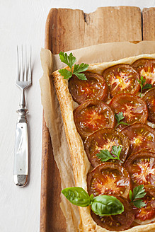 Tarte aus Blätterteig, garniert mit Tomatenscheiben und Kräutern auf einem Schneidebrett - ECF000069