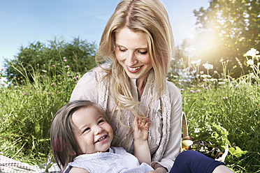 Germany, Cologne, Mother and daughter sitting on meadow, smiling - PDYF000005