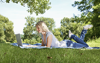 Germany, Cologne, Young woman using laptop in meadow - PDYF000090