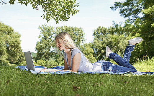 Deutschland, Köln, Junge Frau mit Laptop auf einer Wiese - PDYF000090