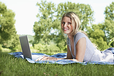 Germany, Cologne, Young woman using laptop in meadow, smiling, portrait - PDYF000091