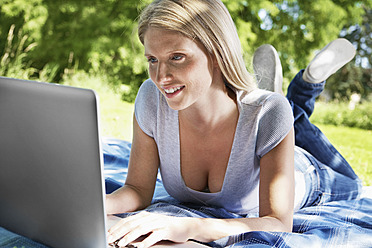 Deutschland, Köln, Junge Frau mit Laptop auf einer Wiese, lächelnd - PDYF000092