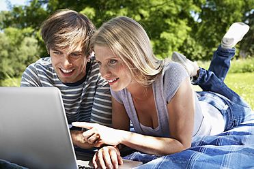 Germany, Cologne, Young couple using laptop in meadow, smiling - PDYF000093