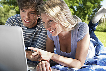 Germany, Cologne, Young couple using laptop in meadow, smiling - PDYF000094