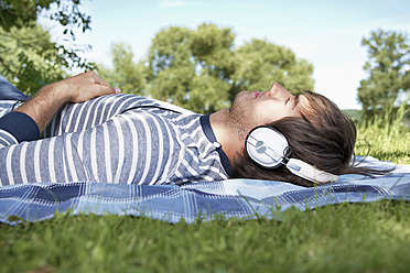 Germany, Cologne, Young man listening music in meadow - PDYF000098