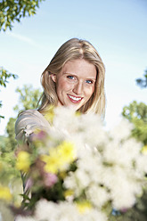 Germany, Cologne, Young woman holding wild flowers, smiling, portrait - PDYF000103