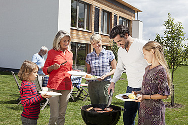 Deutschland, Bayern, Nürnberg, Familie steht um Grill im Garten - RBYF000125