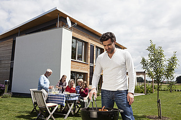 Deutschland, Bayern, Nürnberg, Mann beim Grillen, Familie sitzt im Garten - RBYF000128