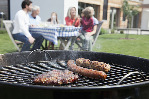 Deutschland, Bayern, Nürnberg, Nahaufnahme eines Grills, Familie sitzt im Hintergrund - RBYF000129