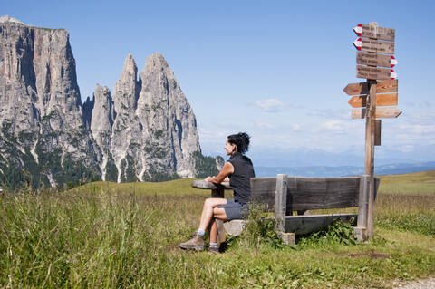 Italien, Mittlere erwachsene Frau sitzt auf einer Bank und blickt zum Schlern in Südtirol, lizenzfreies Stockfoto