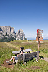 Italien, Mittlere erwachsene Frau sitzt auf einer Bank und blickt zum Schlern in Südtirol - UMF000441