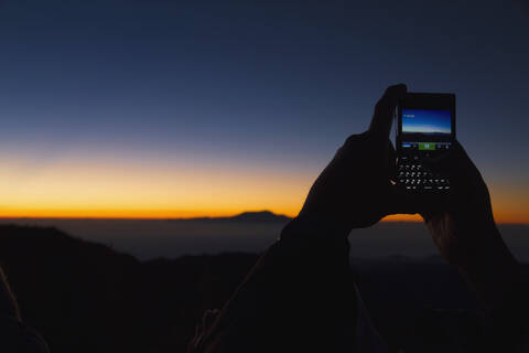 Indonesien, Menschliche Hand beim Fotografieren des Sonnenaufgangs, lizenzfreies Stockfoto