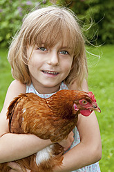 Germany, Brandenburg, Girl holding hen, smiling, portrait - BFRF000019