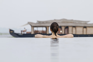 India, Kerala, Young woman in swimming pool looking at houseboat - MBEF000497